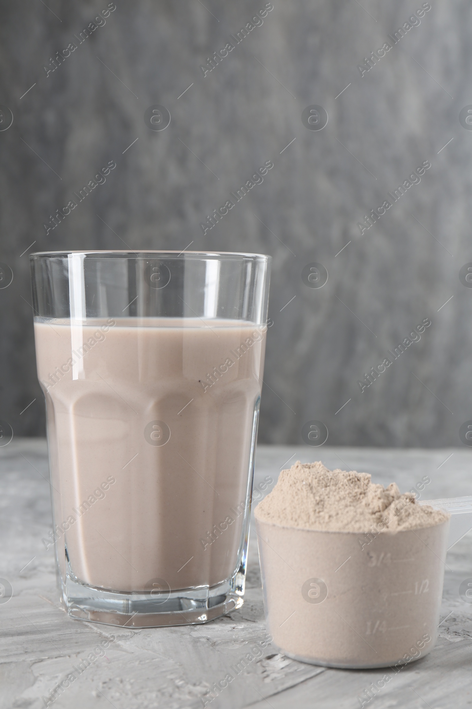 Photo of Delicious protein shake in glass and scoop with powder on grey table