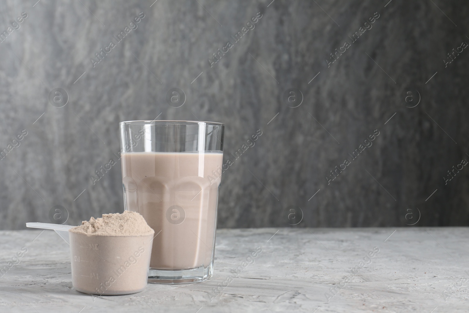 Photo of Delicious protein shake in glass and scoop with powder on grey table, space for text