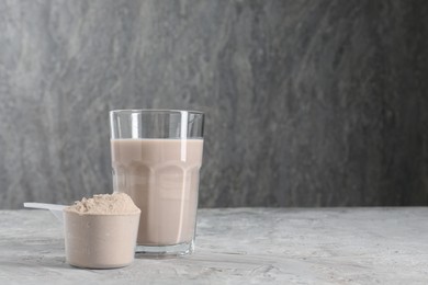 Photo of Delicious protein shake in glass and scoop with powder on grey table, space for text