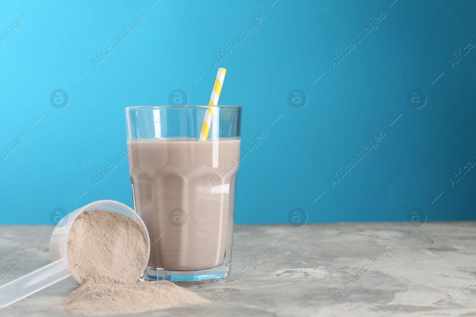 Photo of Delicious protein shake in glass and scoop with powder on grey table, space for text