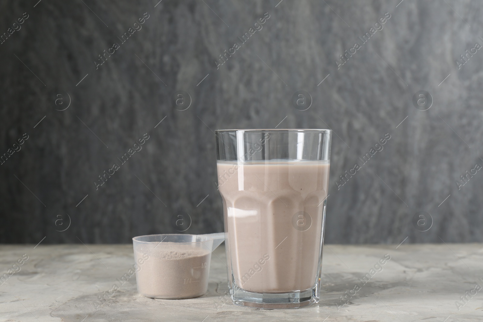 Photo of Delicious protein shake in glass and scoop with powder on grey table