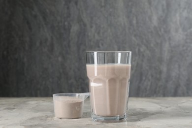 Photo of Delicious protein shake in glass and scoop with powder on grey table