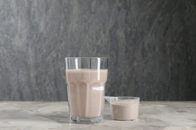 Photo of Delicious protein shake in glass and scoop with powder on grey table