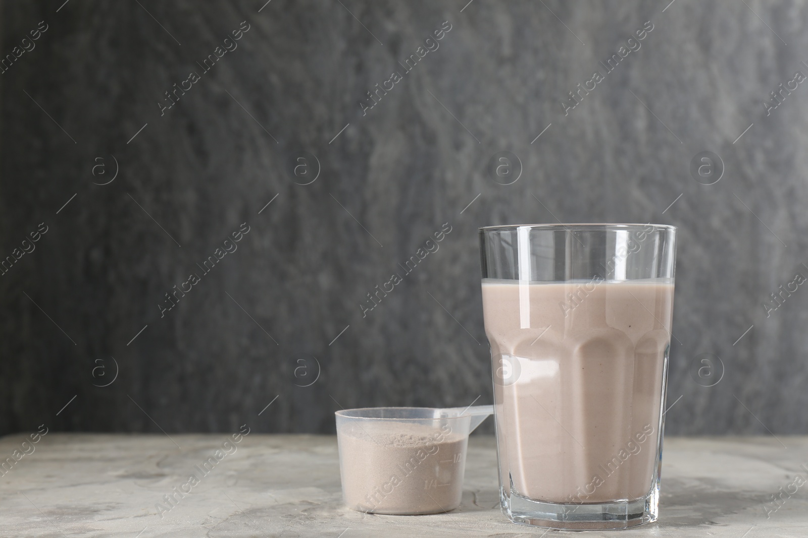 Photo of Delicious protein shake in glass and scoop with powder on grey table, space for text