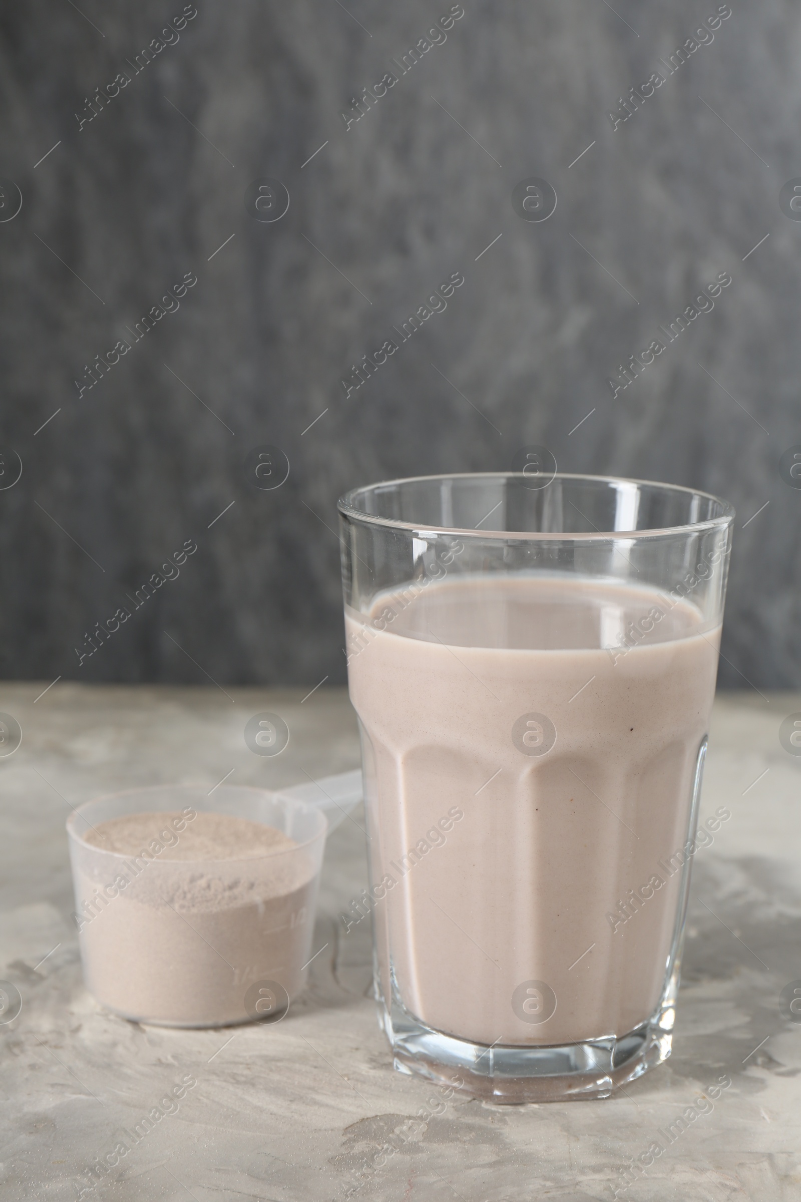 Photo of Delicious protein shake in glass and scoop with powder on grey table