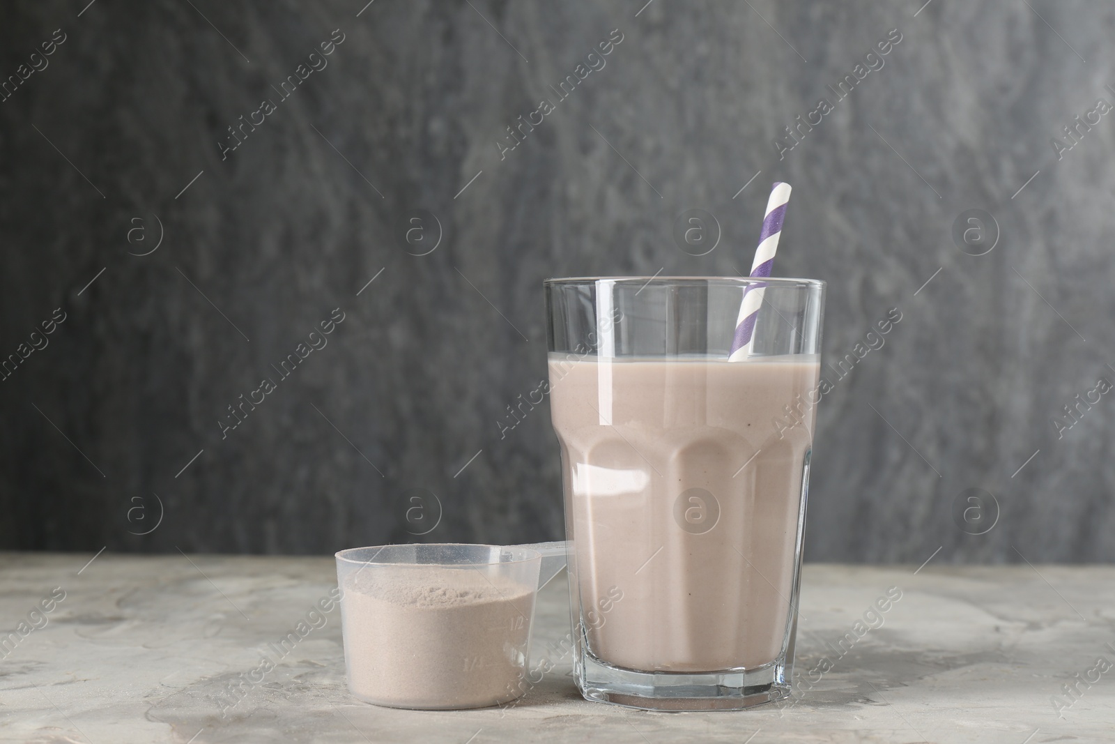 Photo of Delicious protein shake in glass and scoop with powder on grey table