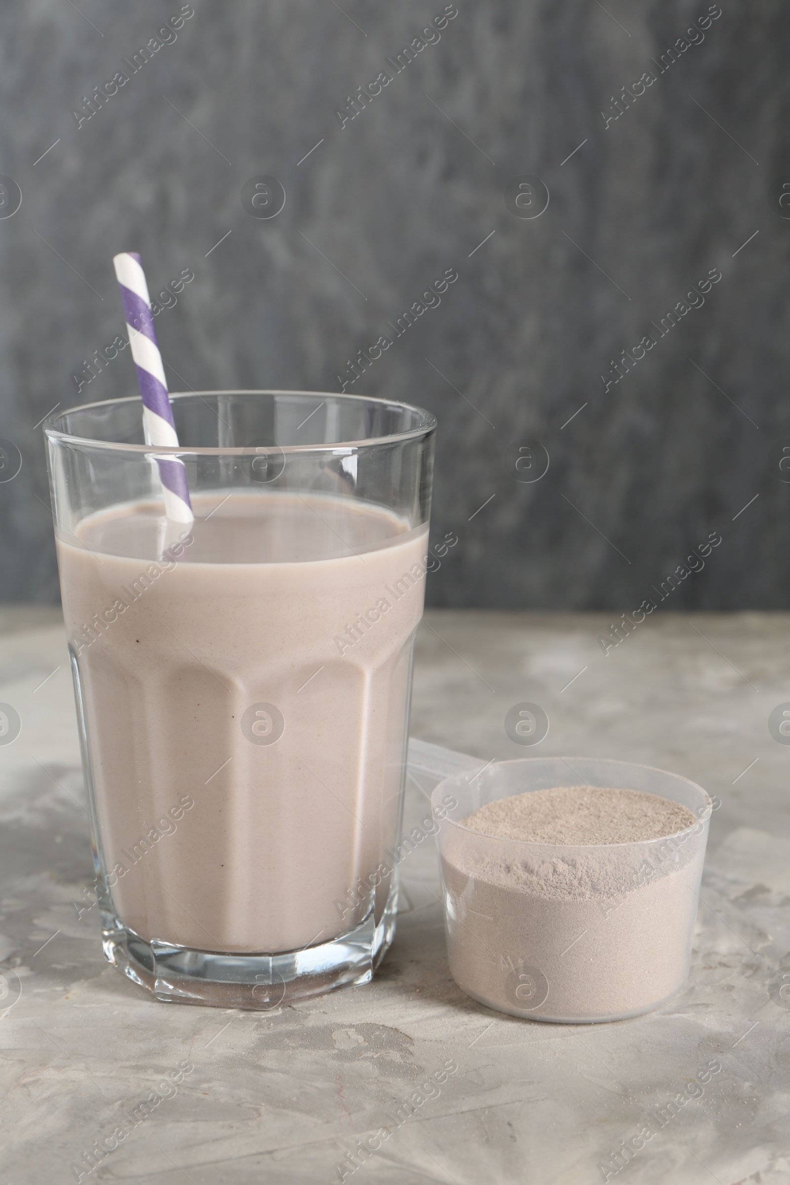 Photo of Delicious protein shake in glass and scoop with powder on grey table