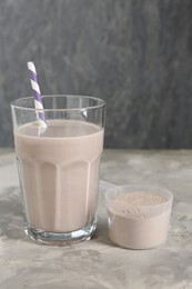 Photo of Delicious protein shake in glass and scoop with powder on grey table