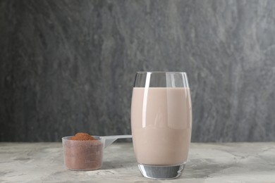 Photo of Delicious protein shake in glass and scoop with powder on grey table