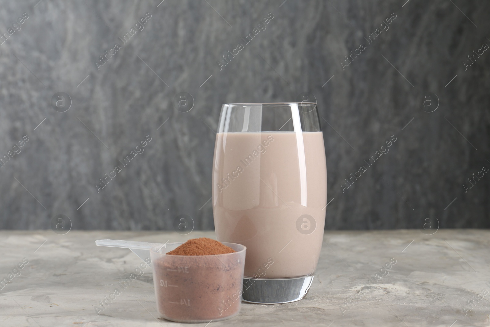 Photo of Delicious protein shake in glass and scoop with powder on grey table