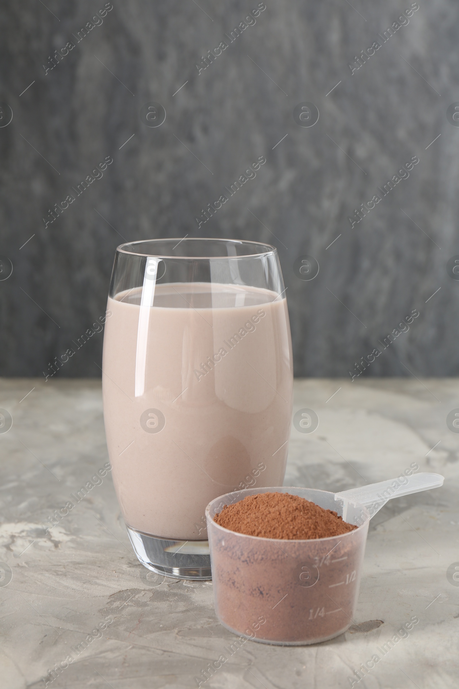 Photo of Delicious protein shake in glass and scoop with powder on grey table