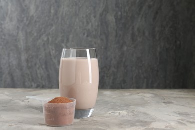 Photo of Delicious protein shake in glass and scoop with powder on grey table, space for text