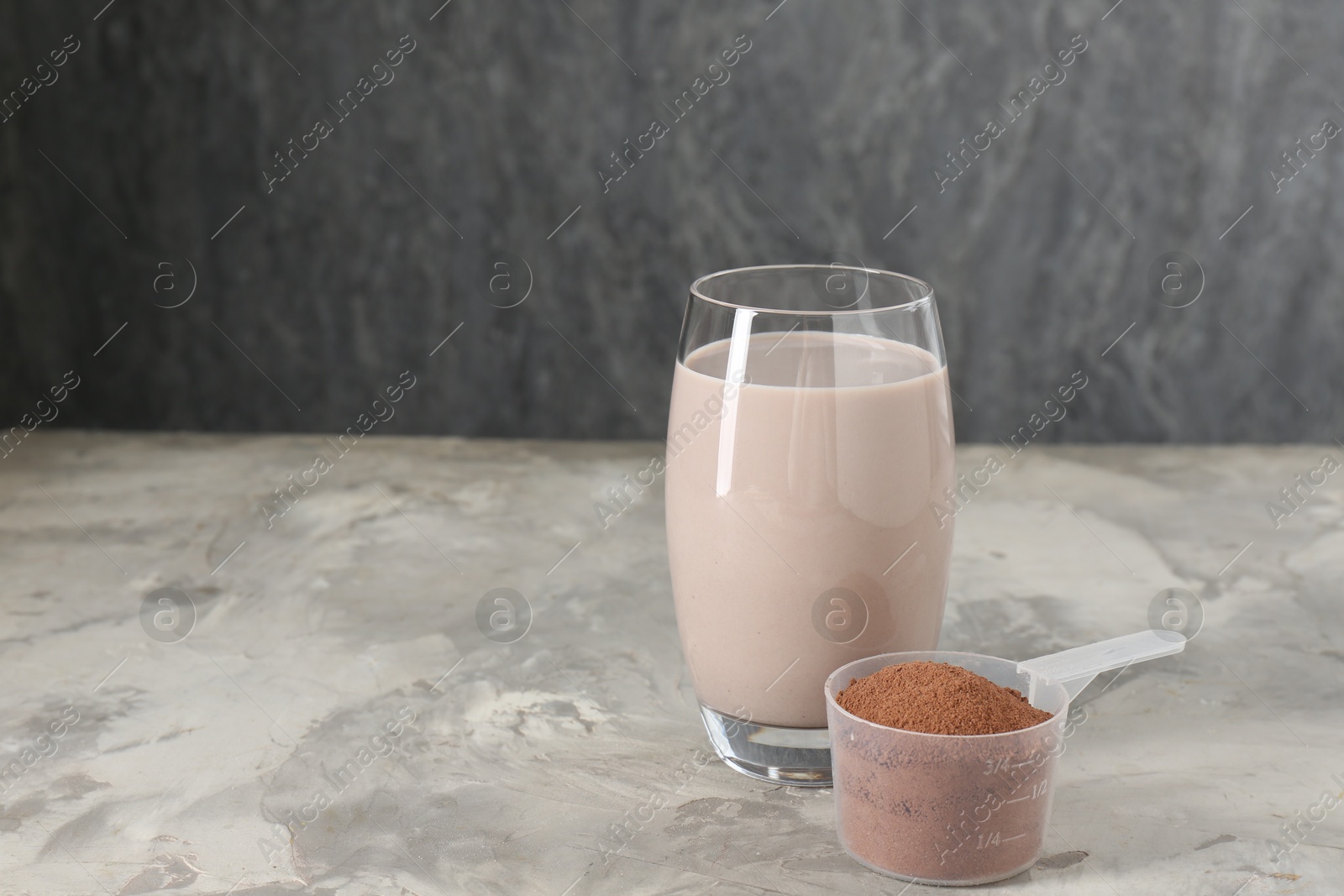 Photo of Delicious protein shake in glass and scoop with powder on grey table, space for text