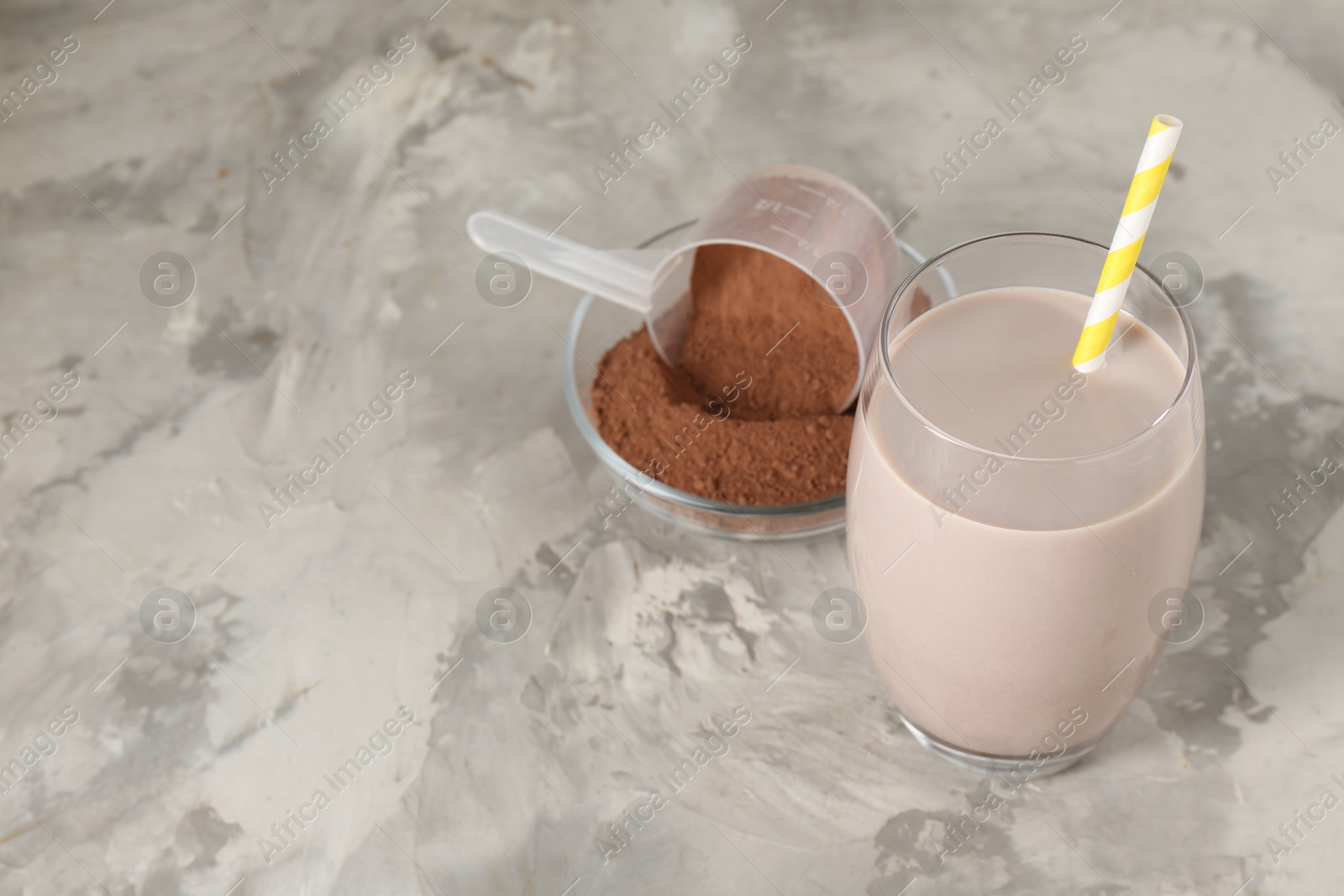 Photo of Delicious protein shake in glass and powder on grey table, closeup. Space for text