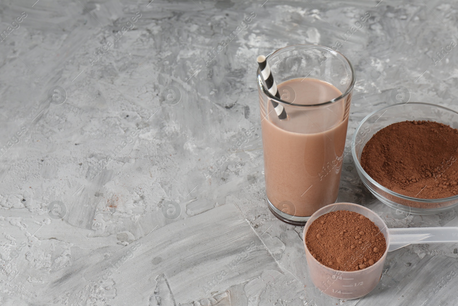 Photo of Delicious protein shake in glass and powder on grey table, space for text