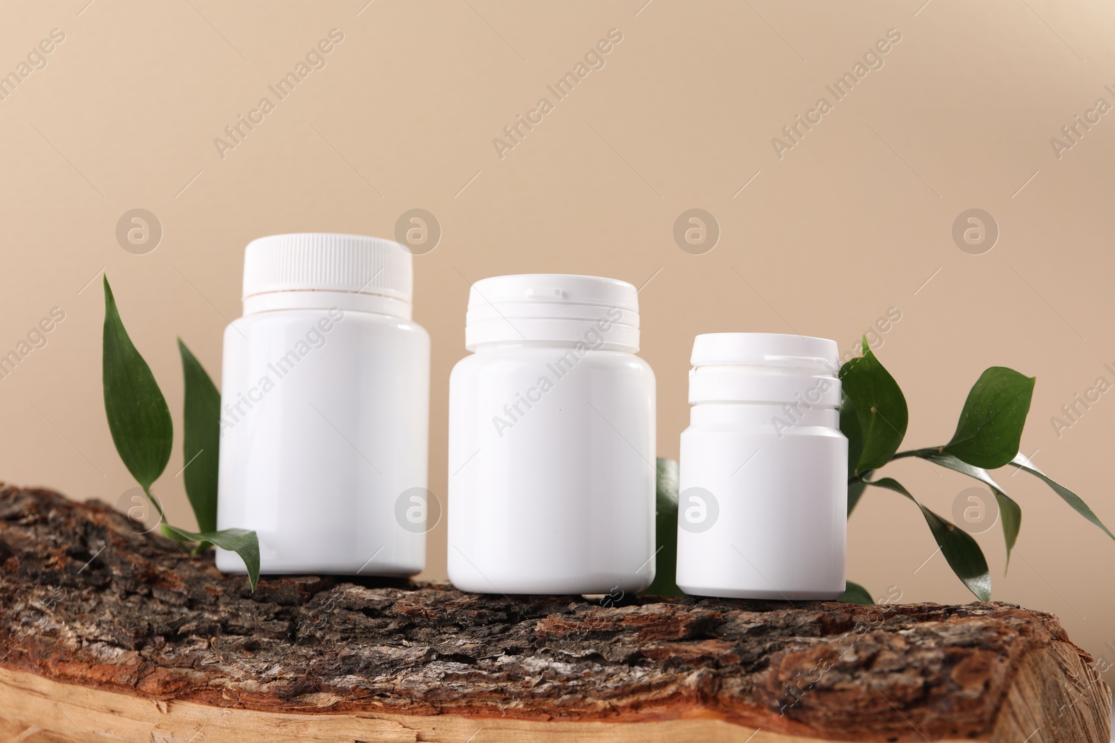 Photo of Plastic medical bottles, green leaves and snag on beige background, closeup