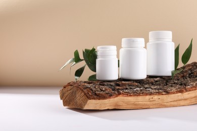 Photo of Plastic medical bottles, green leaves and snag on white table