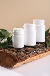 Photo of Plastic medical bottles, green leaves and snag on white table, closeup