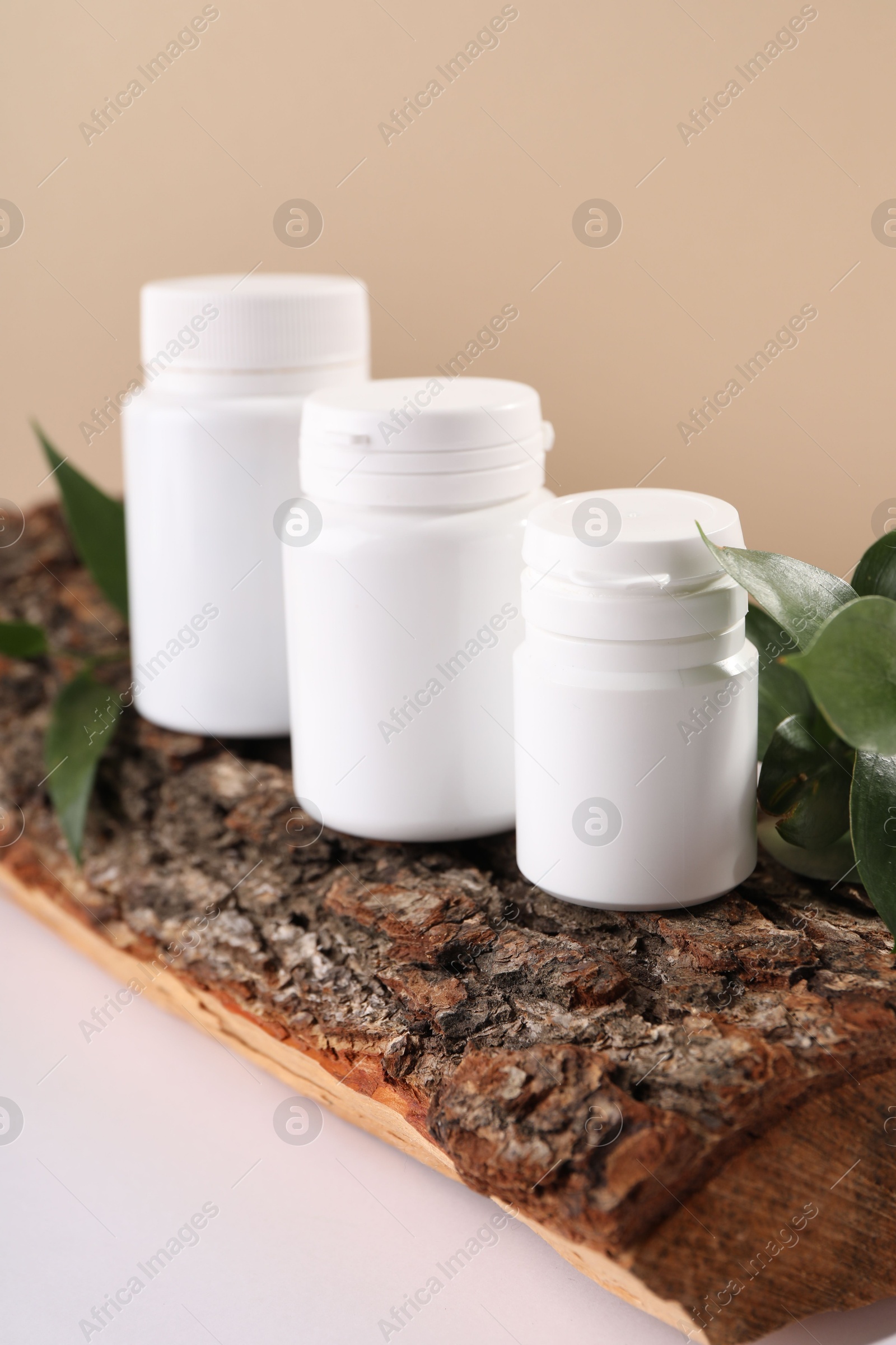 Photo of Plastic medical bottles, green leaves and snag on white table, closeup