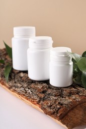 Photo of Plastic medical bottles, green leaves and snag on white table, closeup