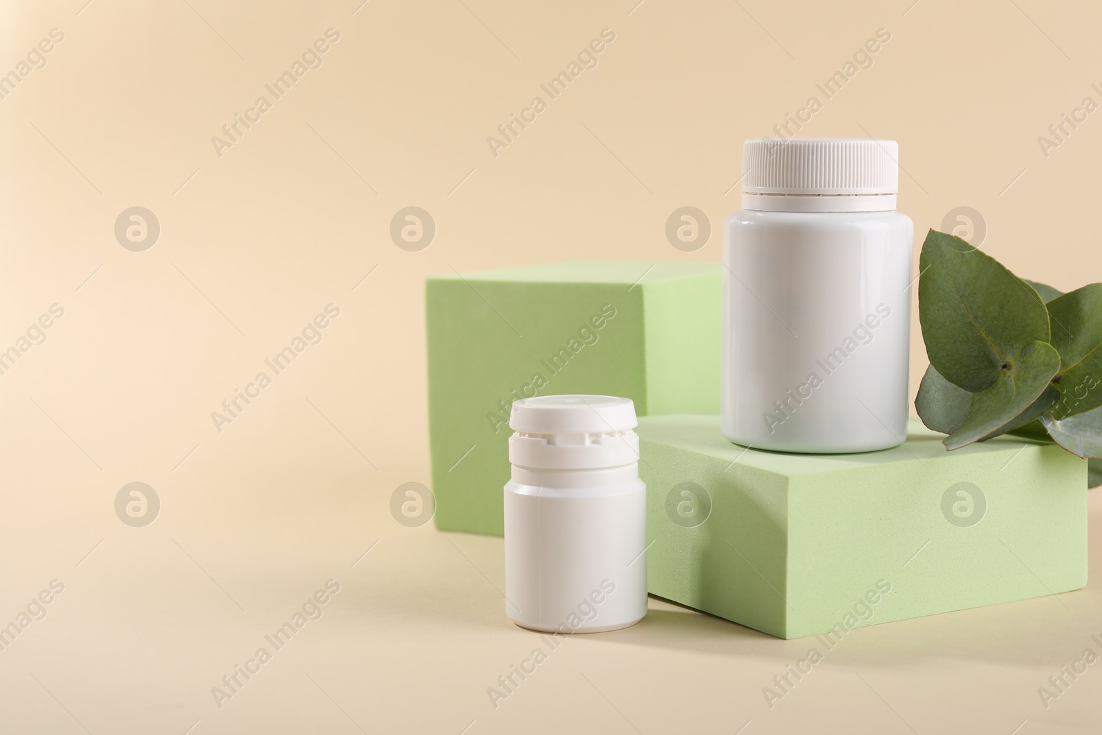 Photo of Plastic medical bottles, eucalyptus leaves and podiums on beige background, space for text