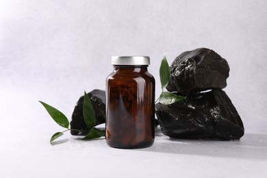 Photo of Medical bottle with pills, green leaves and stones on white textured table