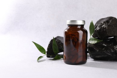 Photo of Medical bottle with pills, green leaves and stones on white textured table