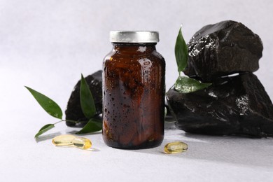 Photo of Medical bottle with pills, green leaves and stones on white textured table