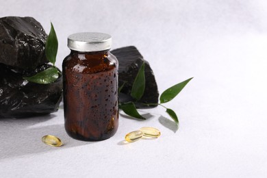 Photo of Medical bottle with pills, green leaves and stones on white textured table, space for text