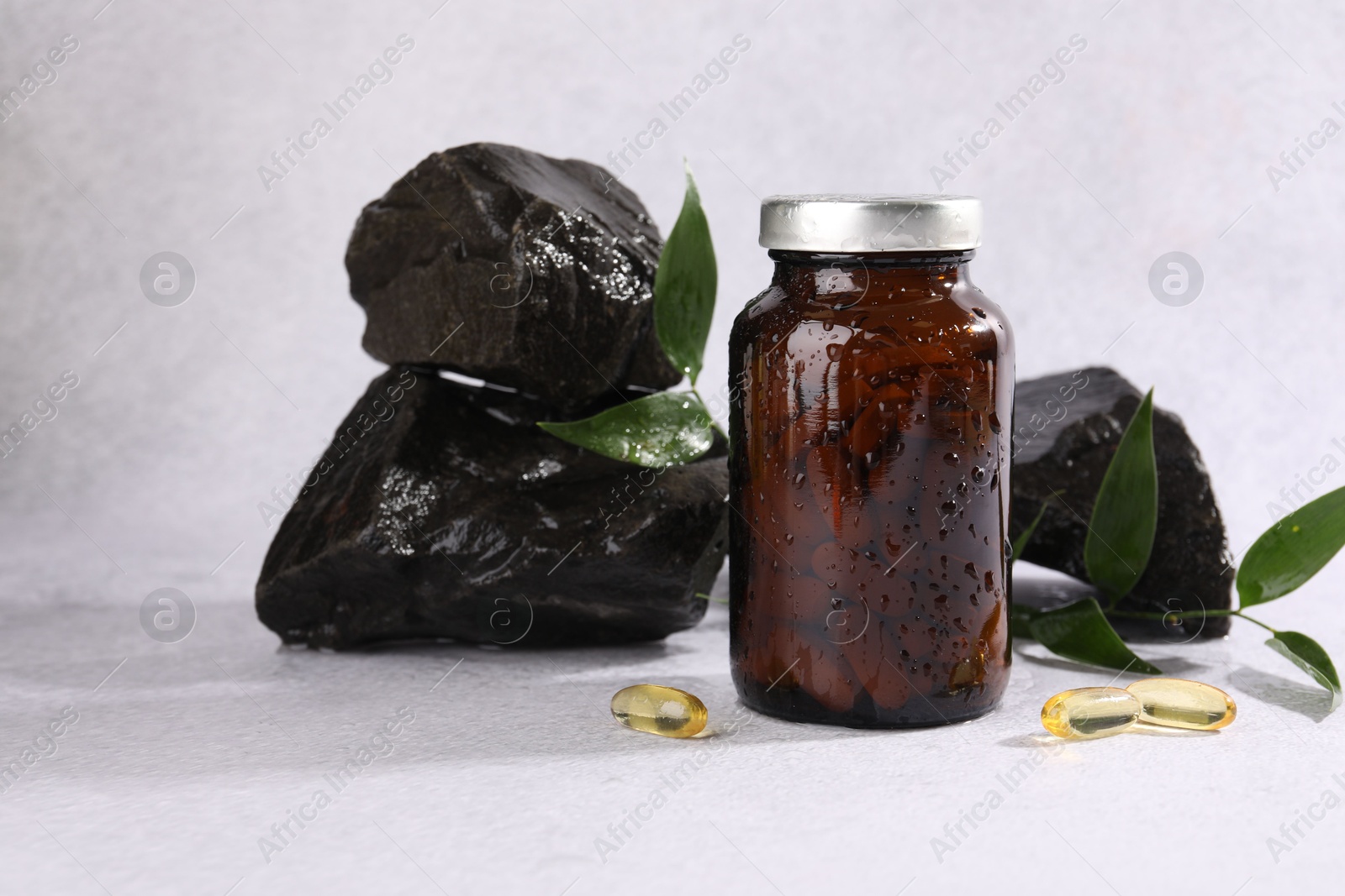 Photo of Medical bottle with pills, green leaves and stones on white textured table