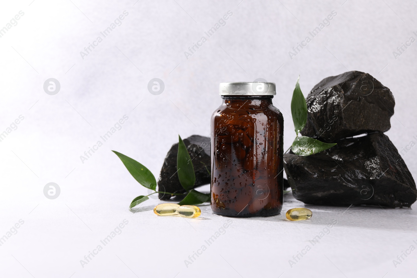 Photo of Medical bottle with pills, green leaves and stones on white textured table, space for text