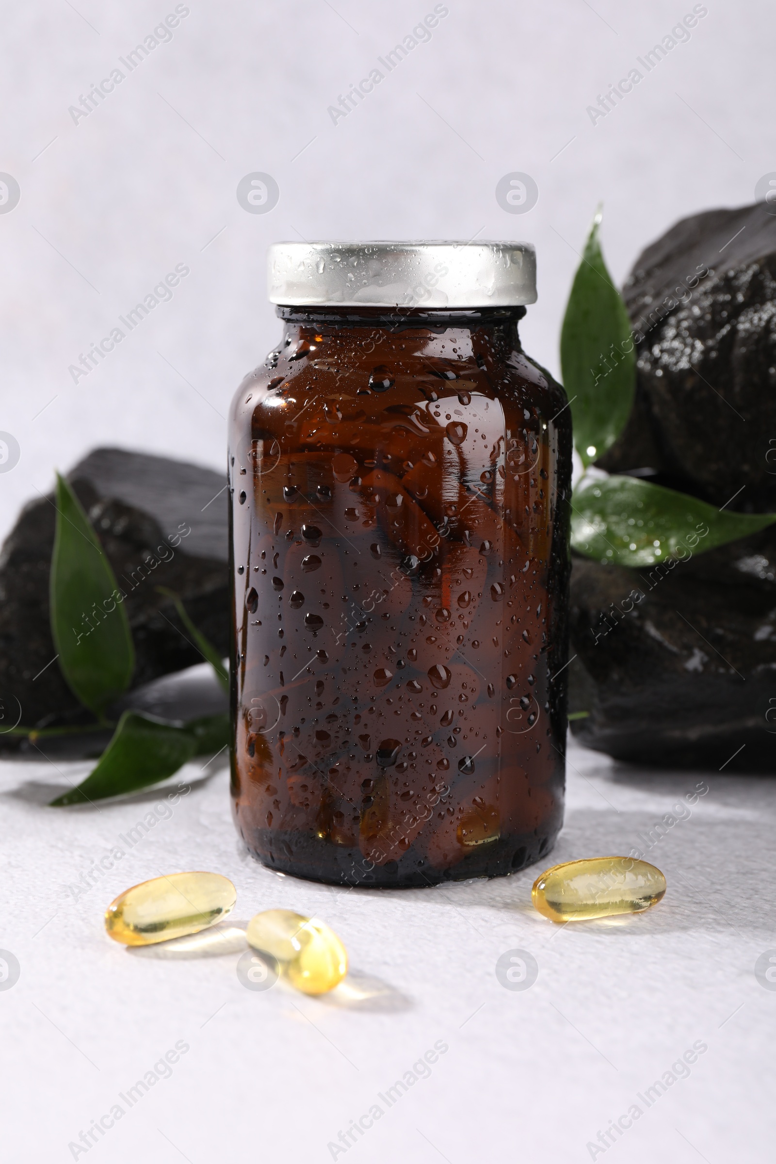 Photo of Medical bottle with pills, leaves and stones on white textured table