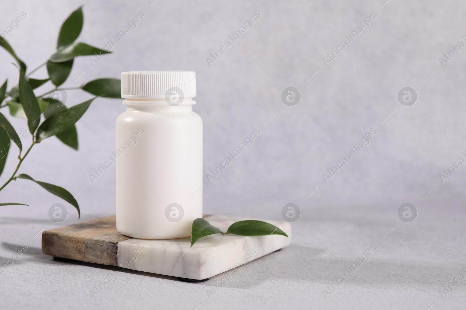 Photo of Plastic medical bottle and green leaves on light grey table, space for text