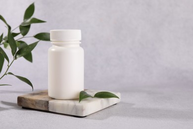 Photo of Plastic medical bottle and green leaves on light grey table, space for text