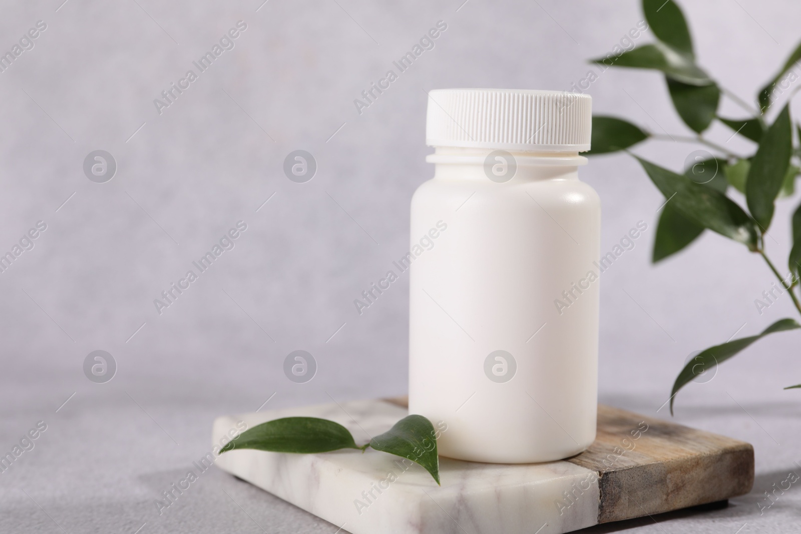 Photo of Plastic medical bottle and green leaves on light grey table, closeup