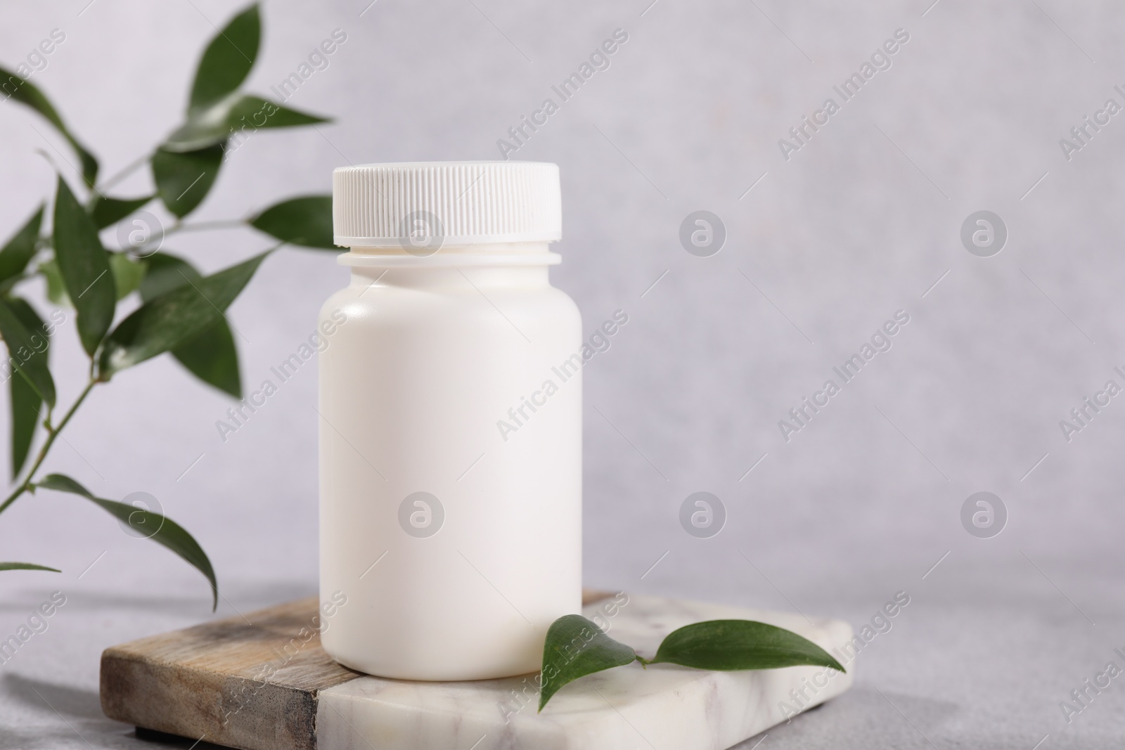 Photo of Plastic medical bottle and green leaves on light grey table, closeup