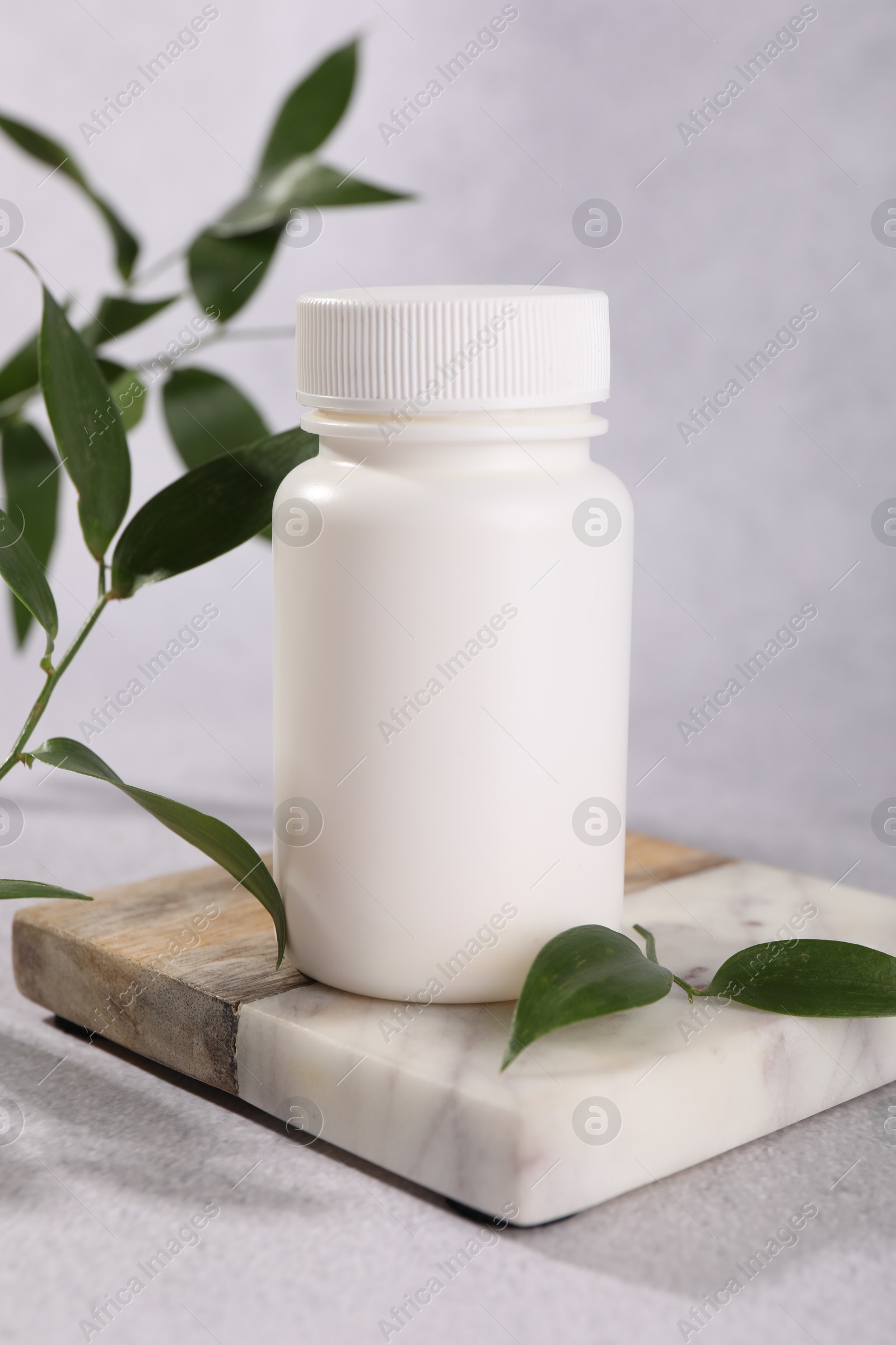 Photo of Plastic medical bottle and green leaves on light grey table