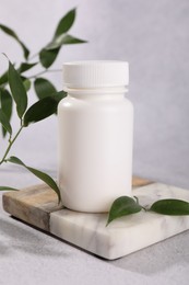 Photo of Plastic medical bottle and green leaves on light grey table