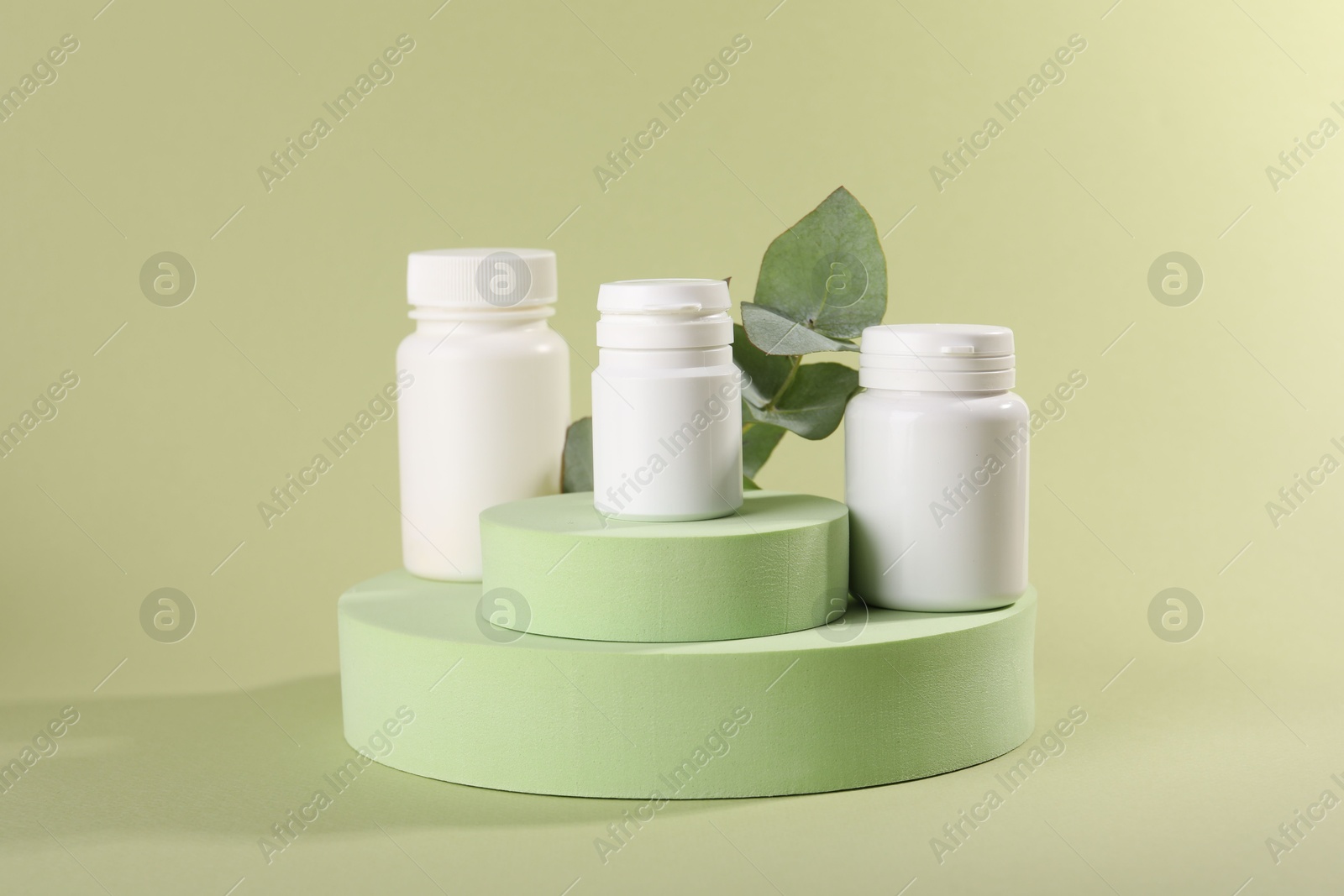 Photo of Plastic medical bottles, leaves and podiums on green background