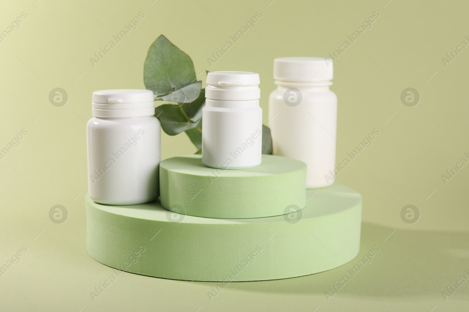 Photo of Plastic medical bottles, leaves and podiums on green background