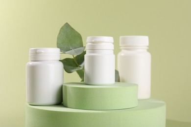 Photo of Plastic medical bottles, leaves and podiums on green background, closeup