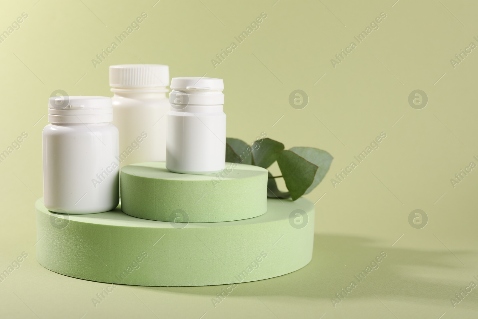 Photo of Plastic medical bottles, leaves and podiums on green background, space for text