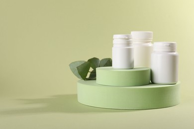 Photo of Plastic medical bottles, leaves and podiums on green background, space for text