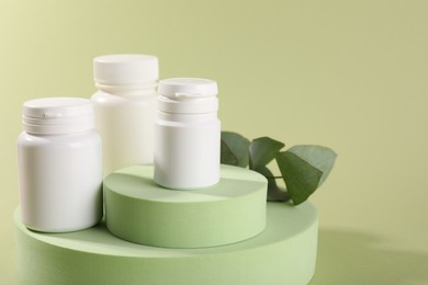 Photo of Plastic medical bottles, leaves and podiums on green background, closeup