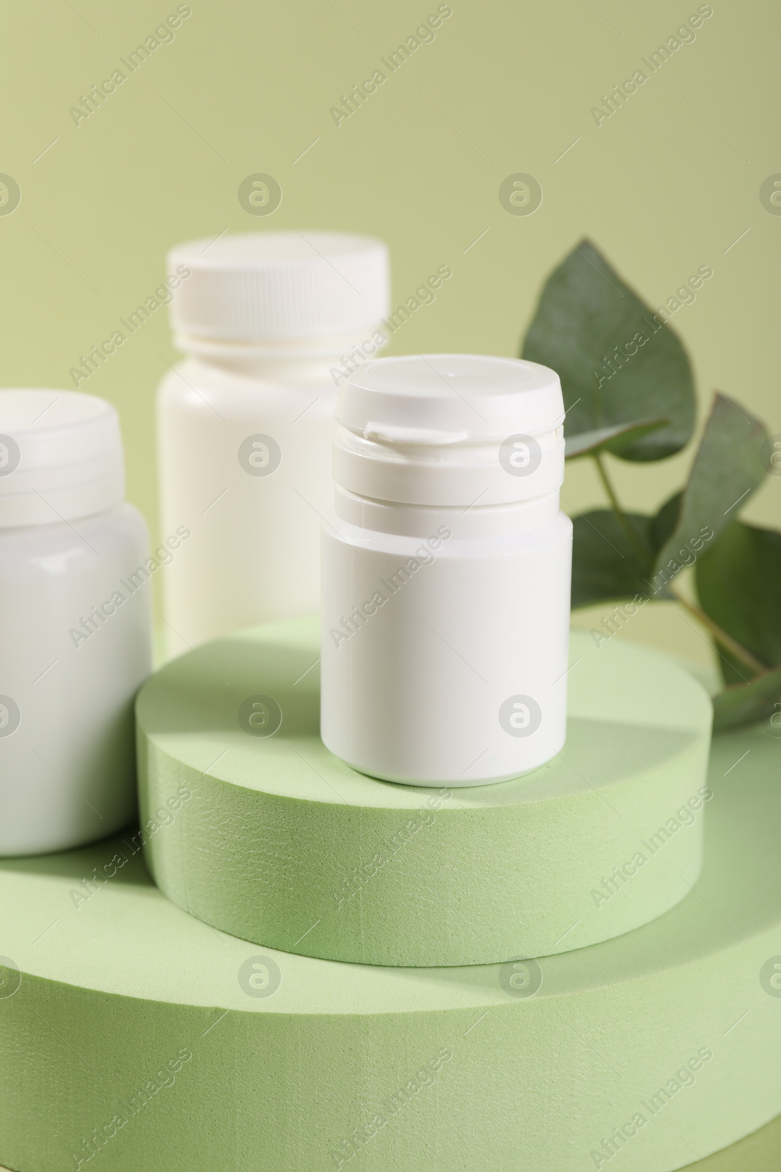 Photo of Plastic medical bottles, leaves and podiums on green background, closeup