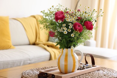 Beautiful ranunculus flowers and chamomiles in vase on table indoors