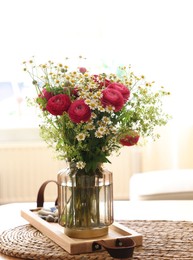 Beautiful ranunculus flowers and chamomiles in vase on table indoors