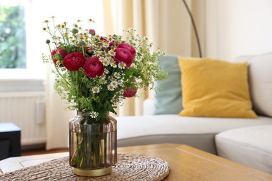 Beautiful ranunculus flowers and chamomiles in vase on table indoors