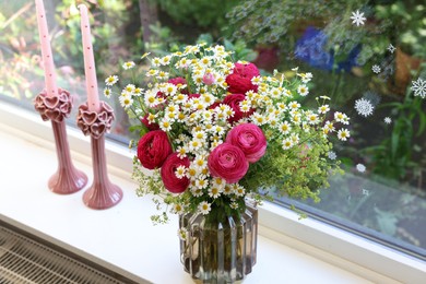 Photo of Beautiful ranunculus flowers and chamomiles in vase on windowsill indoors