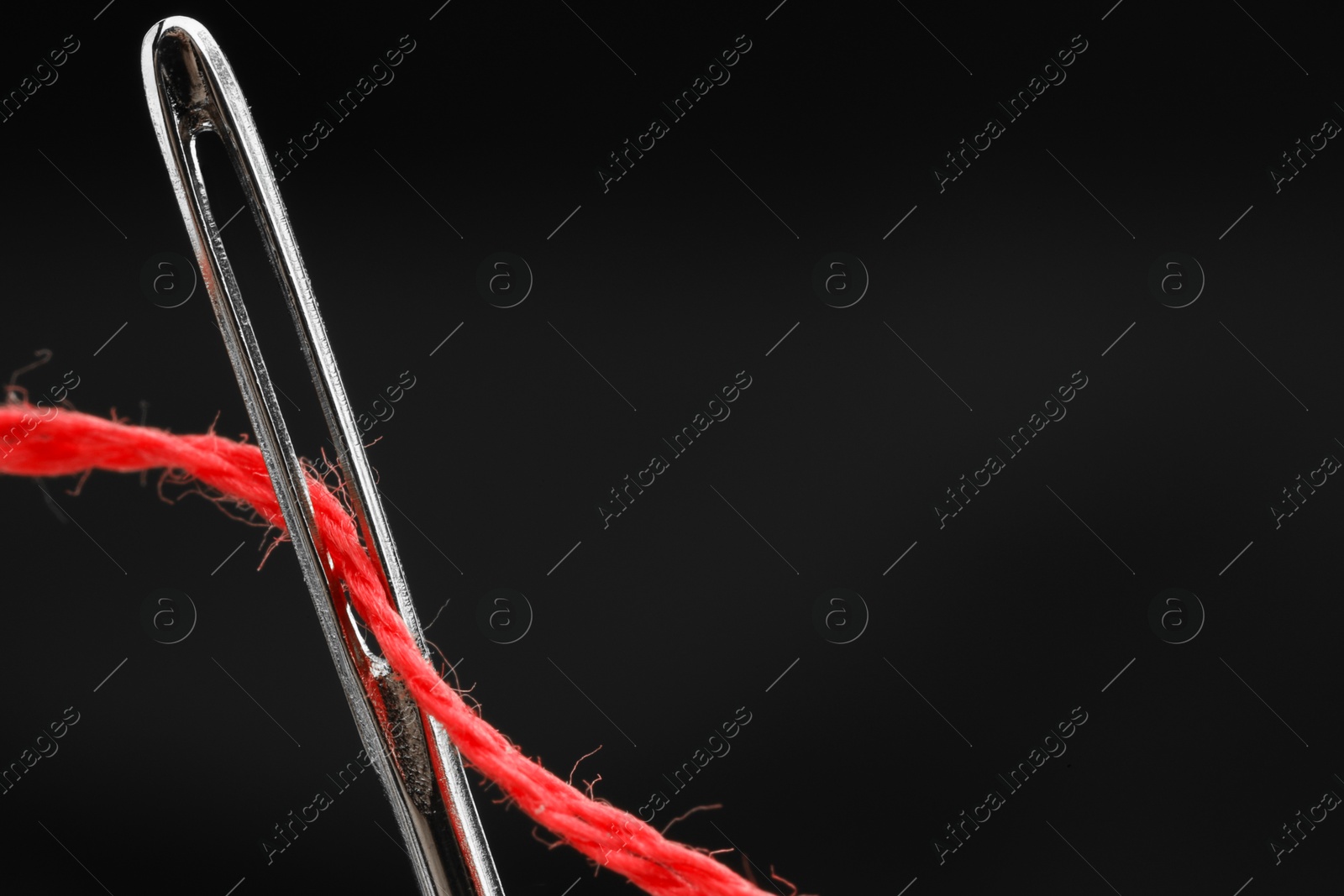 Photo of Sewing needle with red thread on black background, closeup. Space for text